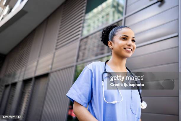 hospital worker standing outside hospital while smiling and looking away. - nurse leaving stock pictures, royalty-free photos & images