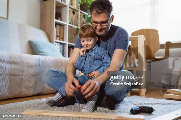 caucasian single father dressing his toddler son, while taking a break from work - electric screwdriver stock pictures, royalty-free photos & images