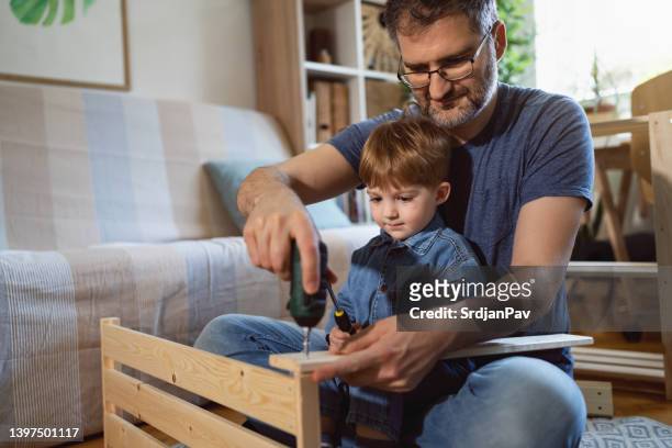 father and son together assembling new wooden furniture - electric screwdriver stock pictures, royalty-free photos & images