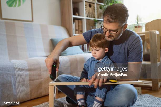 caucasian father and son together assembling new wooden furniture - electric screwdriver stock pictures, royalty-free photos & images