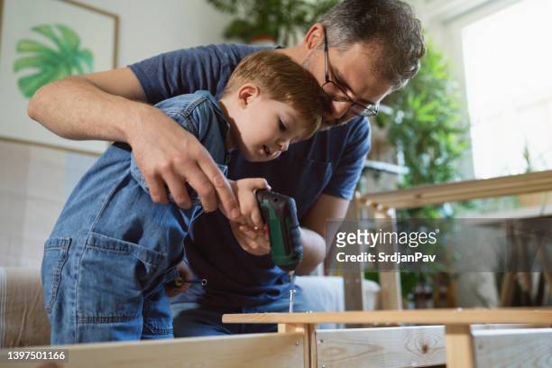 caucasian father and son assembling new wooden furniture while using electric screwdriver - diy kitchen stock pictures, royalty-free photos & images