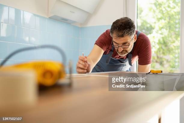 male caucasian carpenter marks the lenght of the kitchen countertop - kitchen straighten stock pictures, royalty-free photos & images
