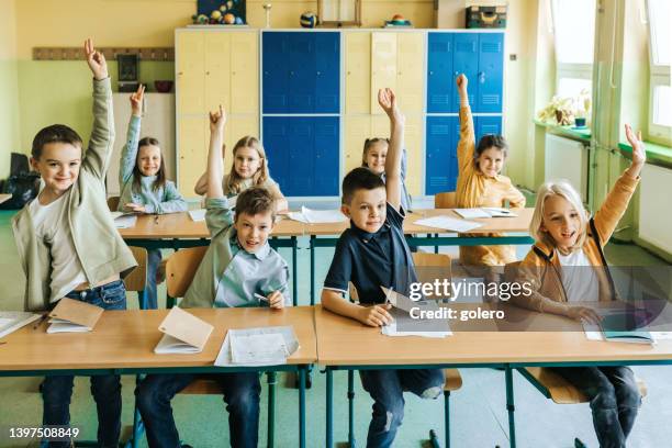 schulkinder im klassenzimmer heben die hände - classroom-front-view stock-fotos und bilder