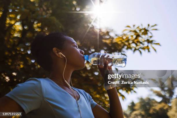 african american woman jogger drinking water hydrating in shade of a tree - shade stock pictures, royalty-free photos & images