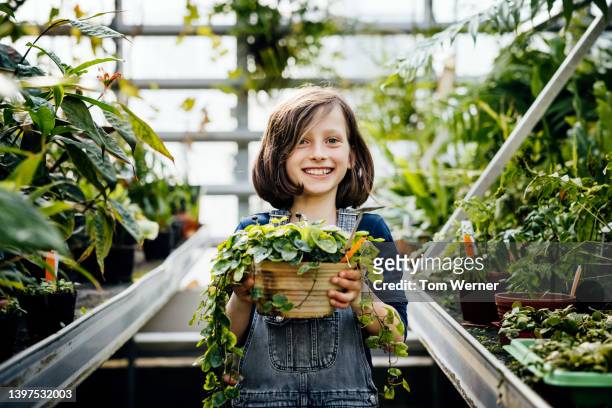 young girl holding plant while exploring greenhouse during field trip - local girls fotografías e imágenes de stock