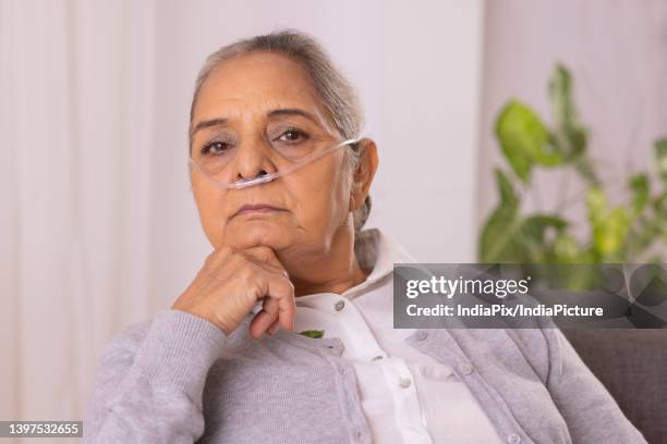 old woman sitting on sofa with nasal cannula at home - nasal cannula ストックフォトと画像