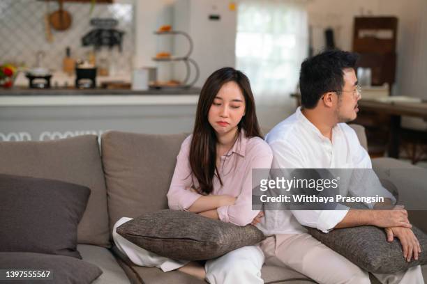 upset couple at home. handsome man and beautiful young woman are having quarrel. sitting on sofa together. family problems. - asian couple arguing stockfoto's en -beelden