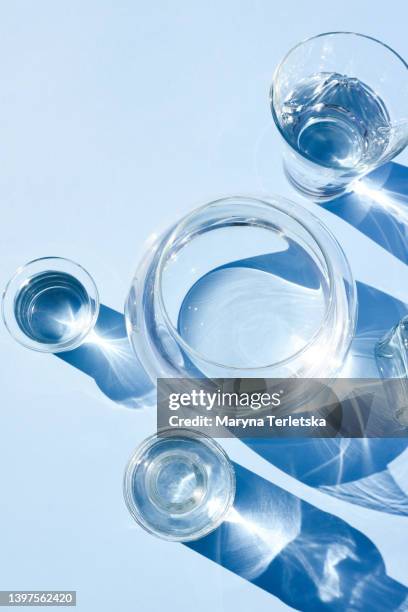 many different vessels with water on a blue background. glassware. minimalism. concept. water balance. liquid. modern composition. - glass water foto e immagini stock