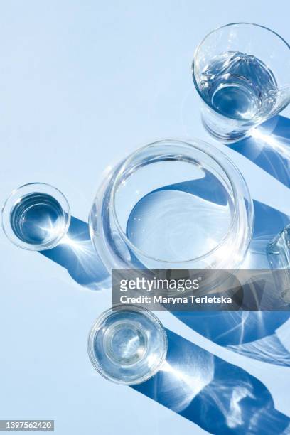 many different vessels with water on a blue background. glassware. minimalism. concept. water balance. liquid. modern composition. - glass shadow stockfoto's en -beelden