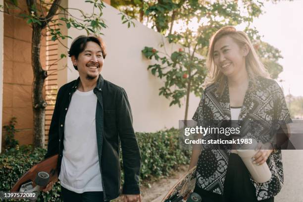 asian couple skateboarder smiling and talking together in the public park. - couple skating stock pictures, royalty-free photos & images