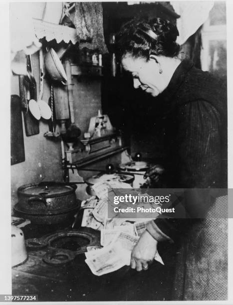 An unidentified woman lights a fire in her kitchen using paper currency, Berlin, Germany, circa 1924. Due to post-WWI inflation, German Marks were...