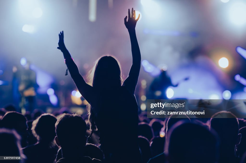 Silhouette of a woman with raised hands on a concert