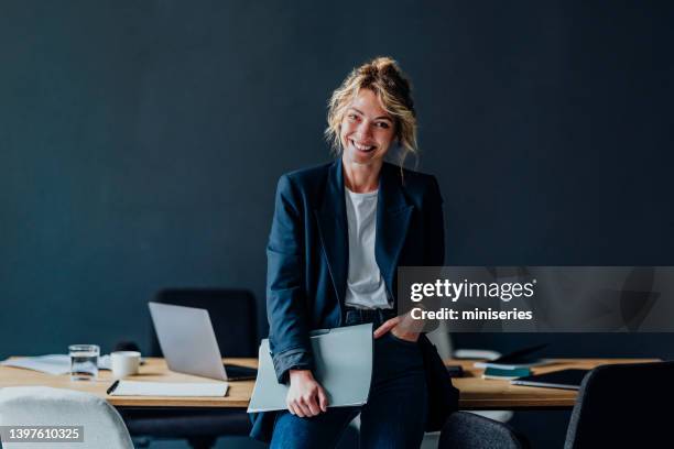 porträt einer lächelnden geschäftsfrau, die im büro steht - corporate dark portrait stock-fotos und bilder