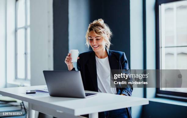 smiling business woman working on a laptop computer in her office - coffee cup disposable stock pictures, royalty-free photos & images