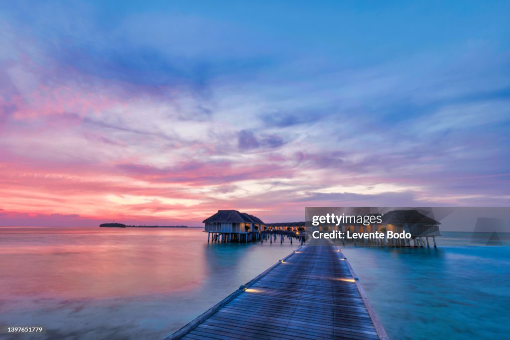 Amazing sunset panorama at Maldives. Luxury resort villas seascape with soft led lights under colorful sky. Beautiful twilight sky and colorful clouds. Beautiful beach background for vacation holiday