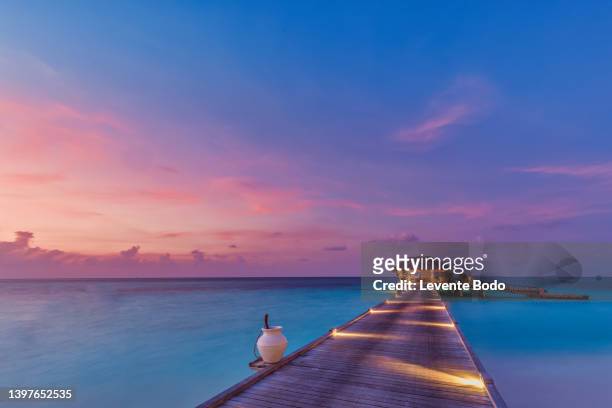 sunset on maldives island, luxury water villas resort and wooden pier. beautiful sky and clouds and beach background for summer vacation holiday and travel concept. paradise sunset landscape - lagune stockfoto's en -beelden