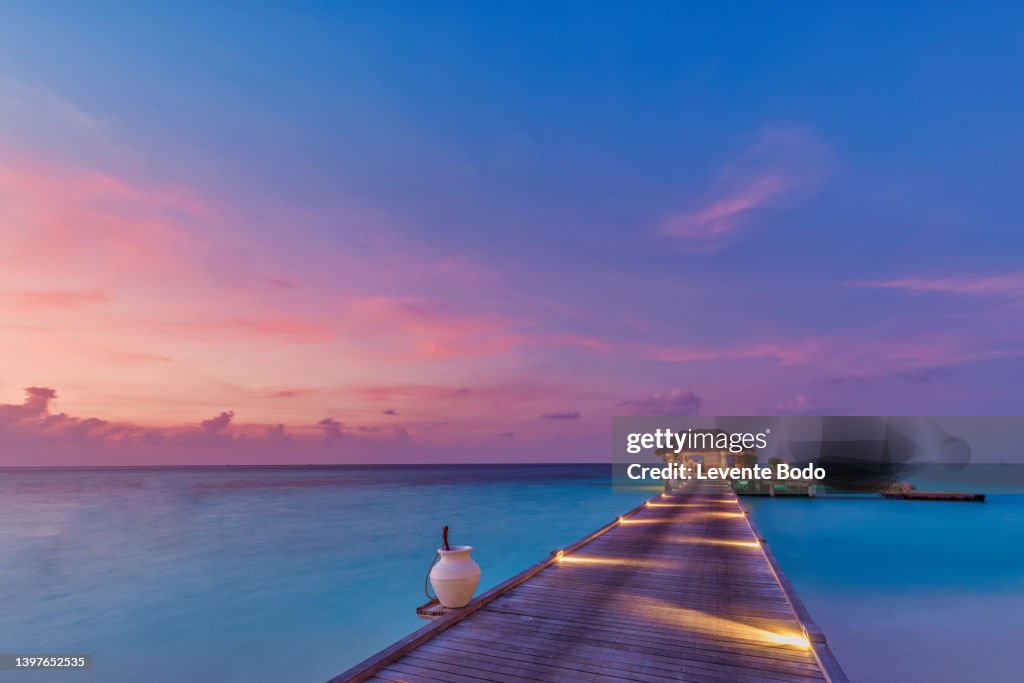 Sunset on Maldives island, luxury water villas resort and wooden pier. Beautiful sky and clouds and beach background for summer vacation holiday and travel concept. Paradise sunset landscape
