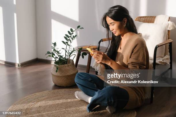 beautiful young woman with brown hair talking on phone, sitting on floor at home. distant work and education. freelanser concept - kazakhstan 個照片及圖片檔