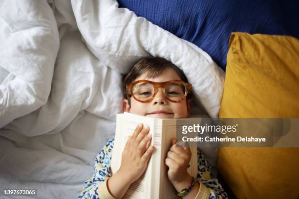 a 4 year old little boy having fun, laying on a bed - kids reading glasses stock pictures, royalty-free photos & images
