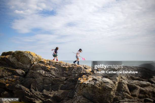 two 6 year old girls walking on rocks, at the seaside - bretagne stockfoto's en -beelden