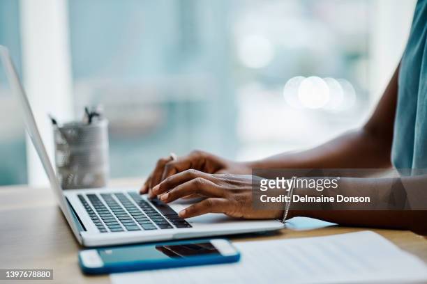 closeup of a black businesswoman typing on a laptop keyboard in an office alone - blogger with laptop stockfoto's en -beelden