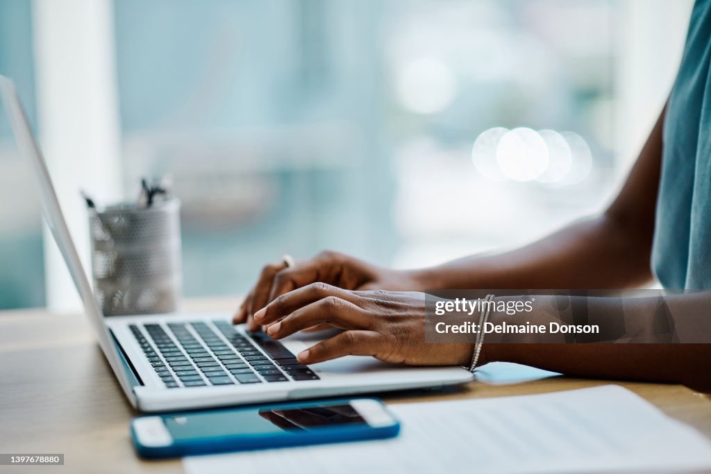 Closeup of a black businesswoman typing on a laptop keyboard in an office alone