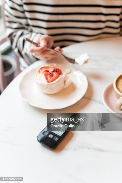diabetic woman eating a meringue cake with her glaucometer on the table in foreground - glaucometer stockfoto's en -beelden