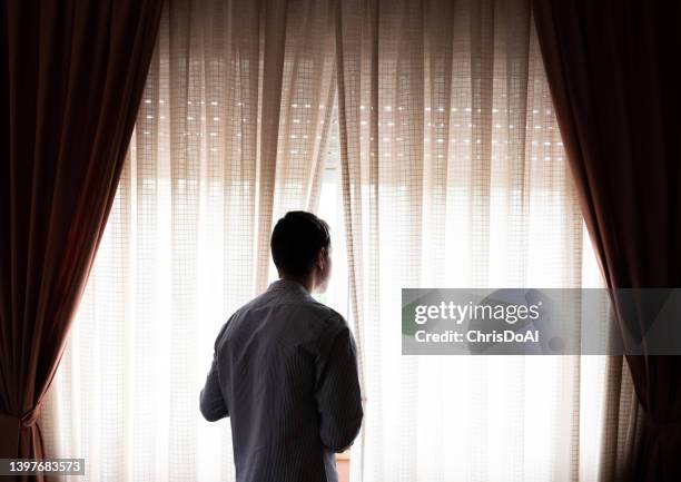 rear view of a man looking through a window - covid stay at home order stock pictures, royalty-free photos & images