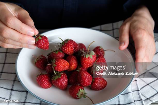red ripe juicy delicious strawberries in a bowl or ceramic plate on a wooden background or table. a woman or a girl has a large berry in her hands, she eats it. the concept of vegetarian, vegan and raw food food and diet. - big country breakfast stock pictures, royalty-free photos & images