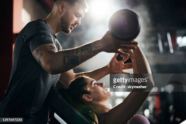 fitness instructor assisting athletic woman in exercising at gym. - gym stock pictures, royalty-free photos & images