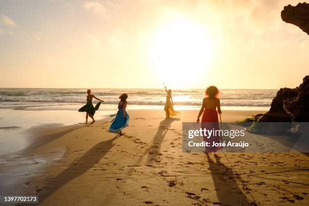 vier feen, die die elemente der natur repräsentieren und bei sonnenuntergang barfuß am strand spazieren gehen - earth wind fire stock-fotos und bilder