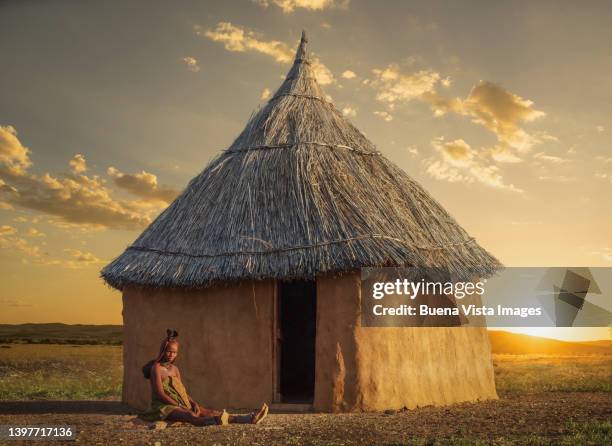 namibia. himba woman sitting near her hut at sunset - opuwo tribe stock-fotos und bilder