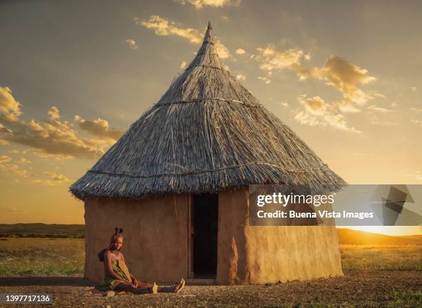 namibia. himba woman sitting near her hut at sunset - opuwo tribe foto e immagini stock