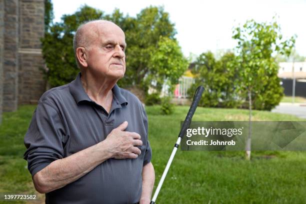 blind man outdoors looking away hand over heart - blind man stockfoto's en -beelden