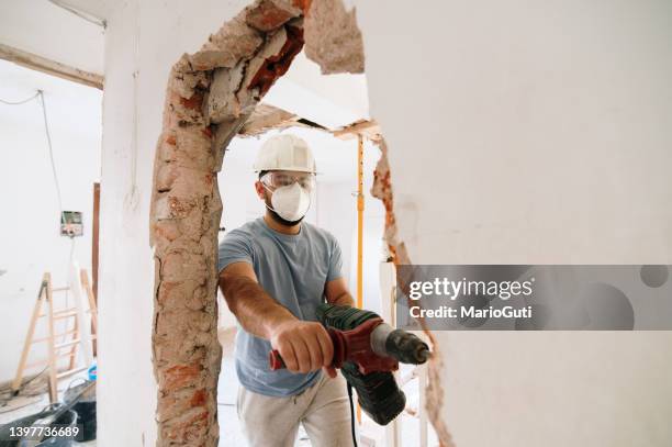 un ouvrier de la construction démolit un mur de briques - destruction photos et images de collection