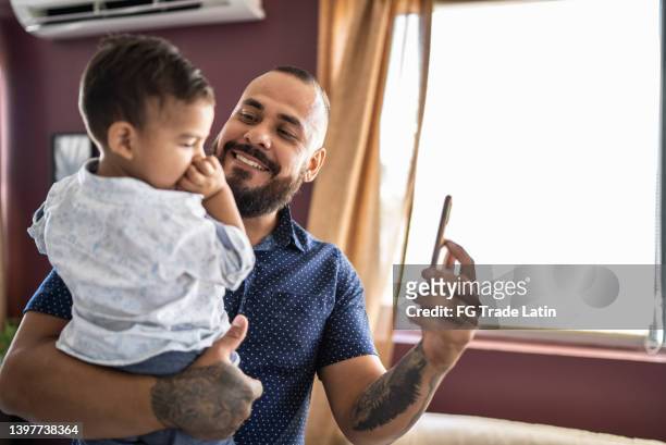 vater und sohn, die zu hause einen videoanruf (oder ein selfie) mit dem mobiltelefon führen - latin father and son stock-fotos und bilder