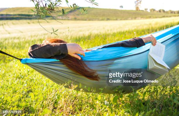 unrecognized relaxed female sleeping in hammock with book in a campsite in nature during a sunny day of summer with copy space. - müde frühling stock-fotos und bilder