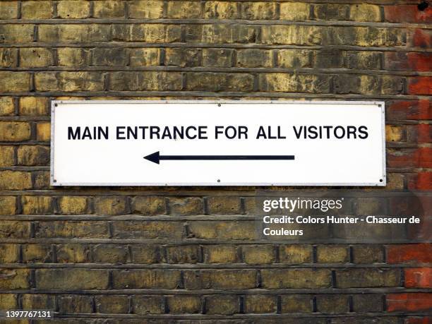 weathered brick wall and sign with an arrow pointing to 'the main entrance for all visitors' in london - panneau d'entrée photos et images de collection