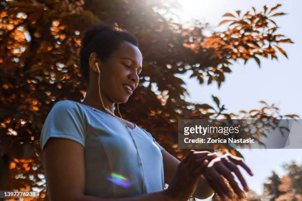 スマートウォッチを見ているスポーツウェアを着た笑顔のアフリカ人女性 - 女性ランナー ストックフォトと画像