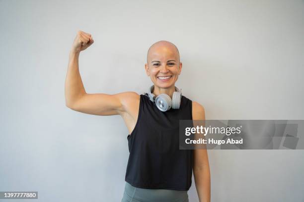 woman smiling and looking at the camera pulling out a ball with her biceps. - resiliencia fotografías e imágenes de stock