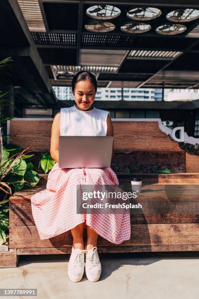 a happy businesswoman working on her computer while sitting on a bench - white skirt stock pictures, royalty-free photos & images