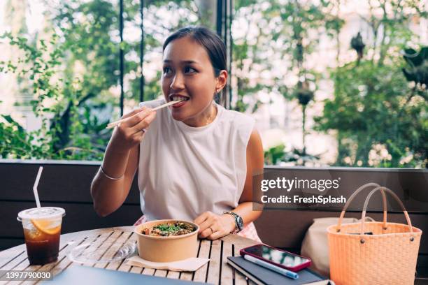 a beautiful businesswoman looking away while having lunch using chopsticks - asians eating stock pictures, royalty-free photos & images