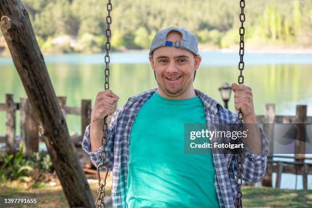 junge mit down-syndrom, der lächelt und schaut auf einer schaukel in die kamera - schaukel stock-fotos und bilder