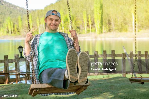 junge mit down-syndrom, der lächelt und schaut auf schaukel in die kamera - schaukel stock-fotos und bilder