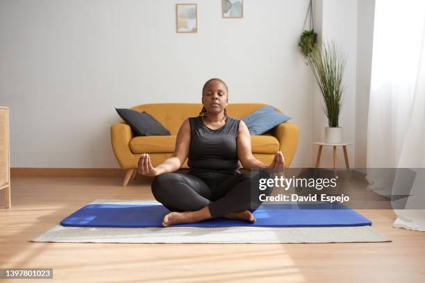 woman sitting on a yoga mat in lotus position while doing a meditation exercise at home. - lotus position imagens e fotografias de stock