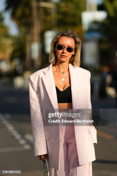 Nataly Osmann wears sunglasses, a necklace, a black crop top / bras, a pastel colored pink oversize blazer jacket, matching suit pants, on May 17,...