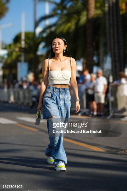 Jessica Wang wears earrings, a white low-neck tank top / crop top, high-waist blue denim ripped jeans pants, a bejeweled shiny bag, white and neon...