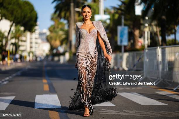 Patricia Gloria Contreras wears earrings, jewelry, a silver shiny long maxi dress with shoulder pads, a corset part, and a see-through lace bottom...