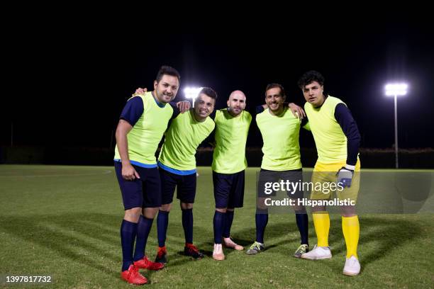 team von fußballspielern beim training, die sich umarmen und in die kamera lächeln - pinafore kleid stock-fotos und bilder