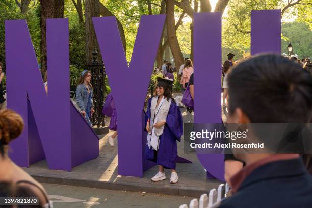 New York University graduate wearing a cap and gown takes photos near a large NYU sign in Washington Square Park on May 17, 2022 in New York City....